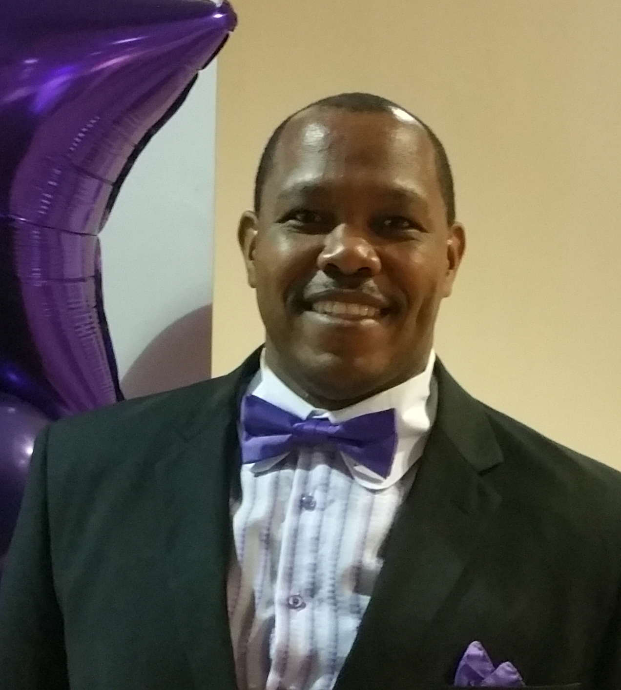 Chris Davios in a formal black tuxedo with purple bow tie, smiling confidently